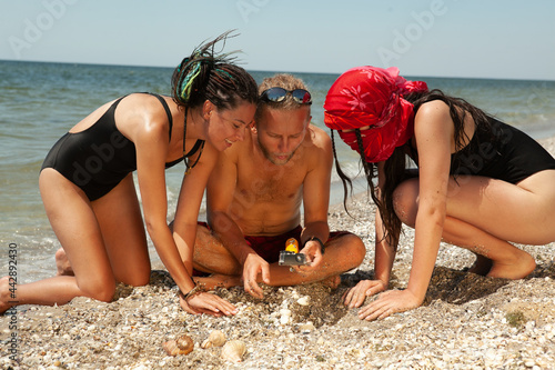 a man with two women are searching in the sand by the sea