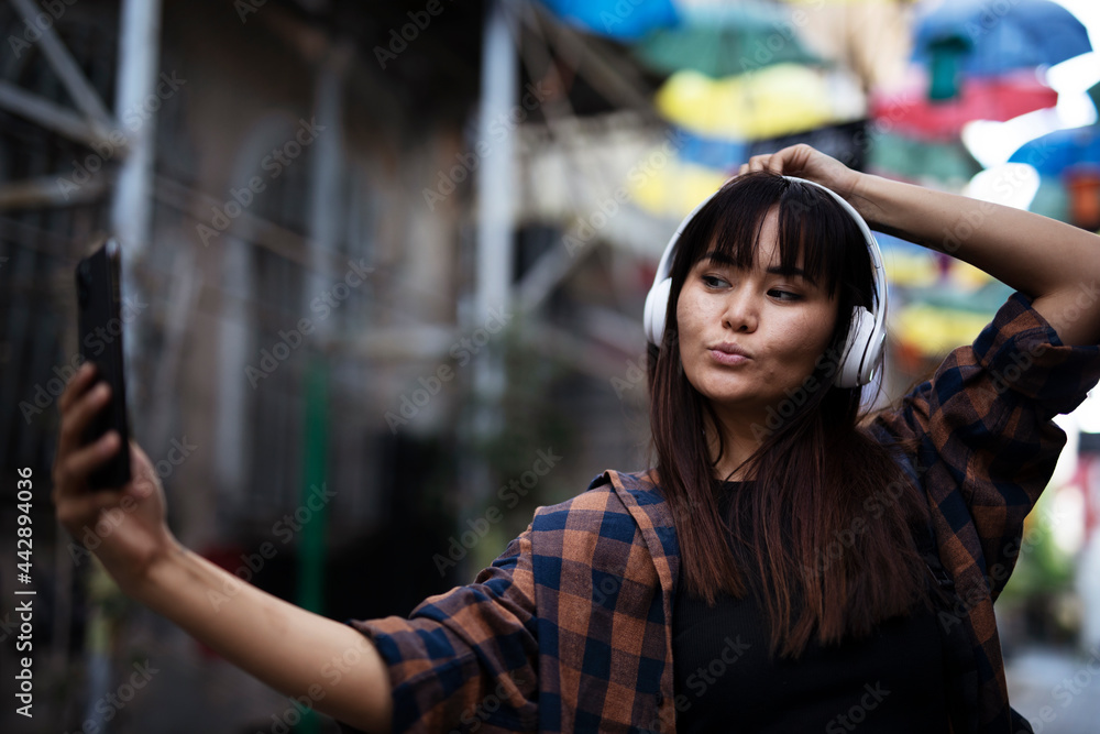 Young smiling woman outdoors. Beautiful woman listening to music while walking through the city..