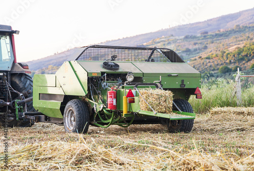 Tractor with harvester attach, harvesting hay crops, creating haystacks on field