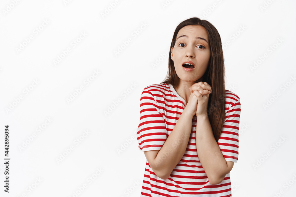 Image of romantic cute girl clench hands, looking with compassion and admiration, touched with smth beautiful, standing over white background in red t-shirt Image of romantic cute girl clench hands, looking with compassion and admiration, touched with smth beautiful, standing over white background in red t-shirt
