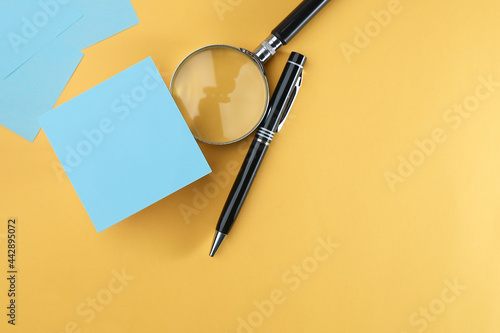 Blank note on the magnifying glass and pen isolated on the yellow background