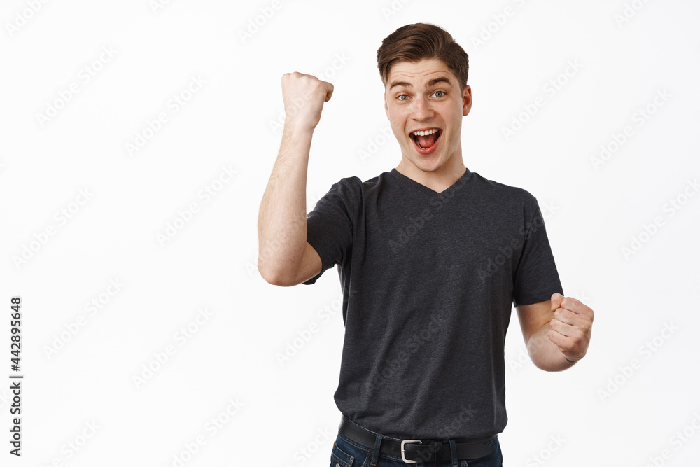 Success. Smiling happy man fist pump, say yes and look excited, winning and celebrating, triumphing from win, enjoy taste of victory, chanting, standing over white background Success. Smiling happy man fist pump, say yes and look excited, winning and celebrating, triumphing from win, enjoy taste of victory, chanting, standing over white background