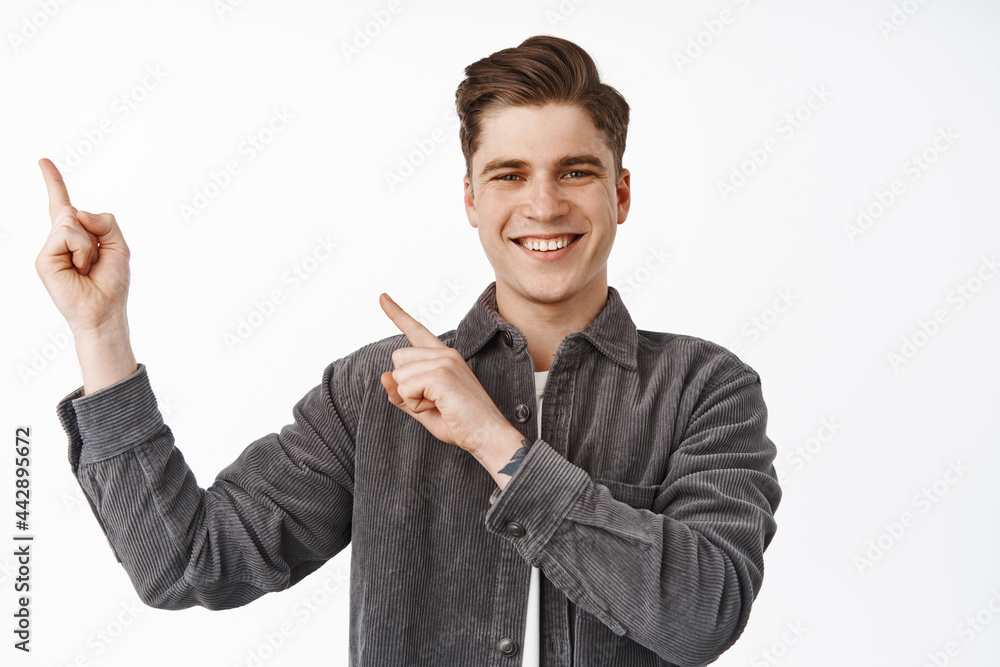 Close up portrait of stylish young man pointing fingers at upper left corner, smiling happy and satisfied, recommending logo, banner or click on link to store, white background Close up portrait of stylish young man pointing fingers at upper left corner, smiling happy and satisfied, recommending logo, banner or click on link to store, white background