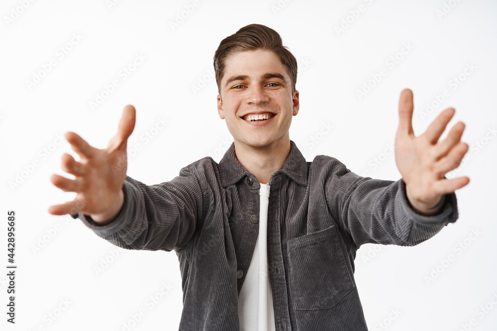 Portrait of smiling happy young man reaching for hugs, stretch out hands and looking friendly, embracing welcoming, wanting to hold take something in his arms, white background Portrait of smiling happy young man reaching for hugs, stretch out hands and looking friendly, embracing welcoming, wanting to hold take something in his arms, white background