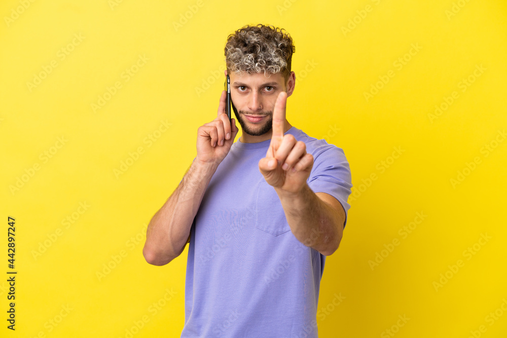 Young caucasian man using mobile phone isolated on yellow background showing and lifting a finger Young caucasian man using mobile phone isolated on yellow background showing and lifting a finger