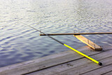 A yellow rod lying on a stand on a wooden bridge by a river. Fishing equipment.