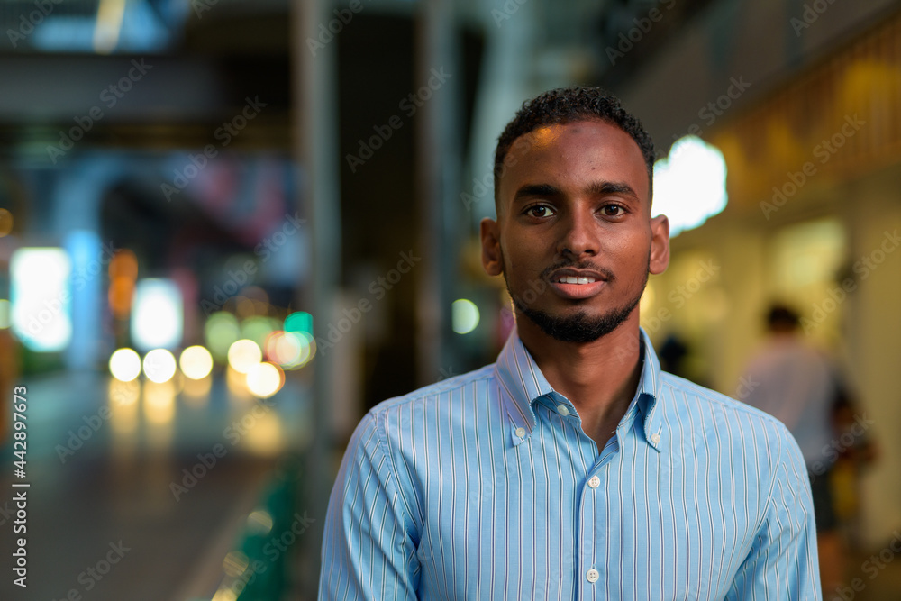 Portrait of handsome black African businessman outdoors in city at night smiling