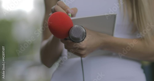 Female journalist at news event writing notes, holding microphone photo