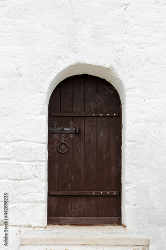 Old vintage brown wooden door in old white stone wall. Front view. © mark_ka