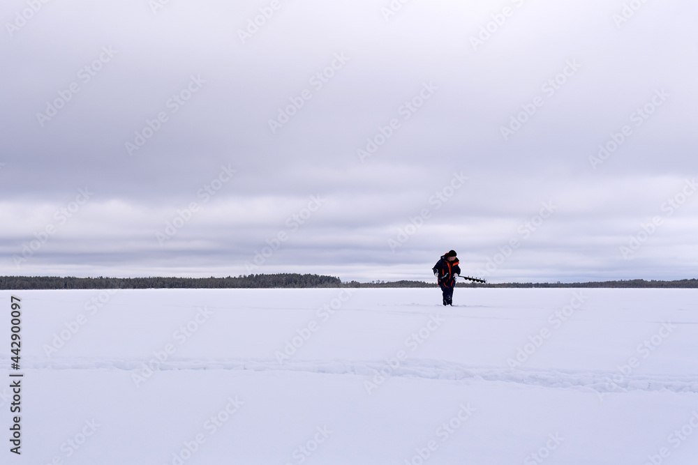 fisherman on a winter lake drills the ice with a motor drill