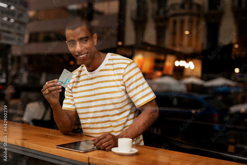Handsome young african man in cafe drinking coffee. Portrait of happy man with credit card drinking coffee in cafe