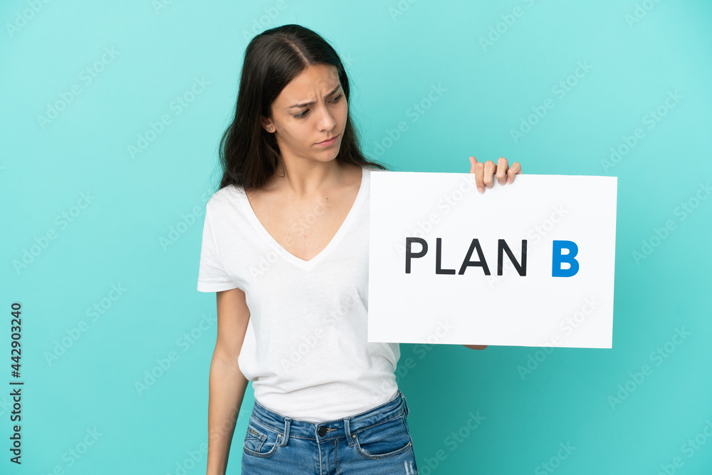 Young French woman isolated on blue background holding a placard with the message PLAN B with sad expression Young French woman isolated on blue background holding a placard with the message PLAN B with sad expression
