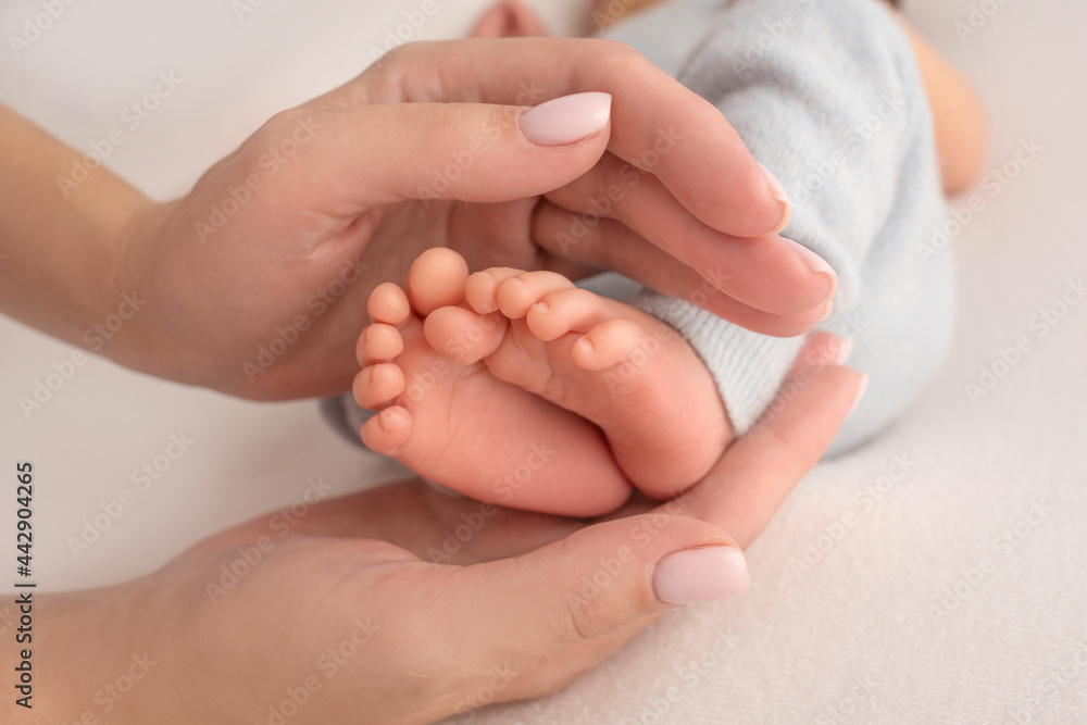 Female hands of young mother holding her newborn baby feet, closeup image with blur baby in background Female hands of young mother holding her newborn baby feet, closeup image with blur baby in background