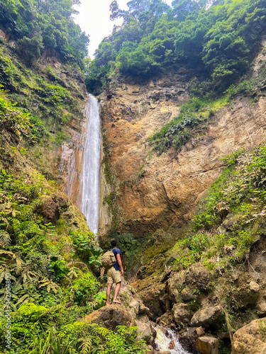 Young adventurous guy standing in front of a huge wild waterfall in Azores islands.