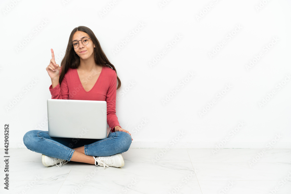 Young French girl sitting on the floor with her laptop pointing with the index finger a great idea Young French girl sitting on the floor with her laptop pointing with the index finger a great idea