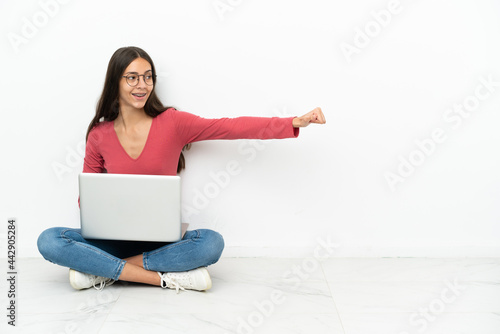 Young French girl sitting on the floor with her laptop giving a thumbs up gesture © luismolinero