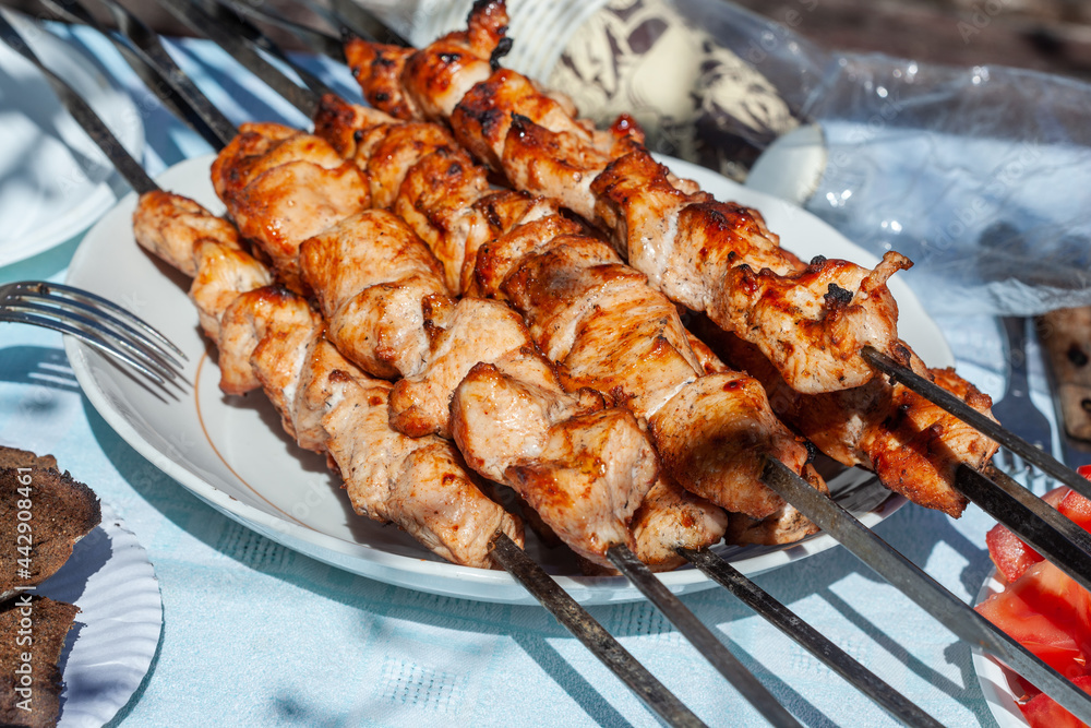 freshly cooked chicken skewers lying in a disposable plastic plate with fried bread
