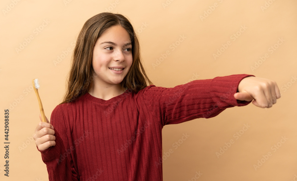 Little caucasian girl brushing her teeth isolated on beige background giving a thumbs up gesture Little caucasian girl brushing her teeth isolated on beige background giving a thumbs up gesture