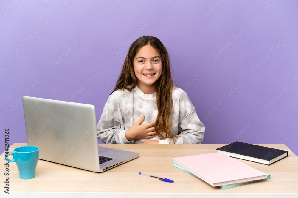 Little student girl in a workplace with a laptop isolated on purple background smiling a lot Little student girl in a workplace with a laptop isolated on purple background smiling a lot