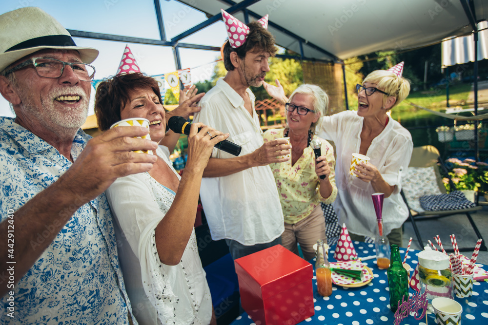 Senior people celebrating birthday in the cottage on the river singing karaoke.
