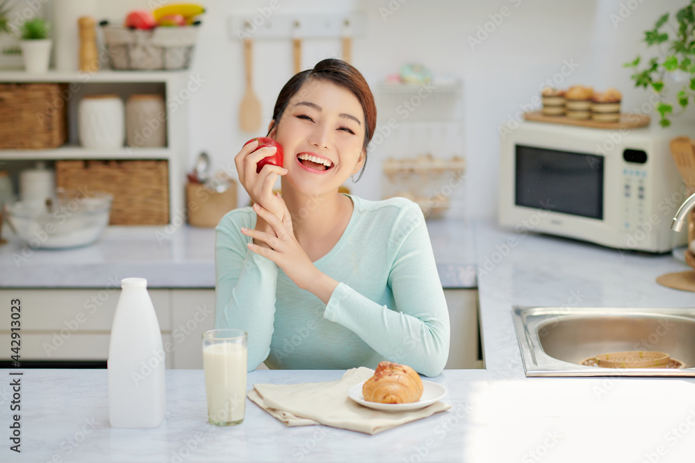 Smiling happy woman eating fresh apple for breakfast while sitting in a kitchen