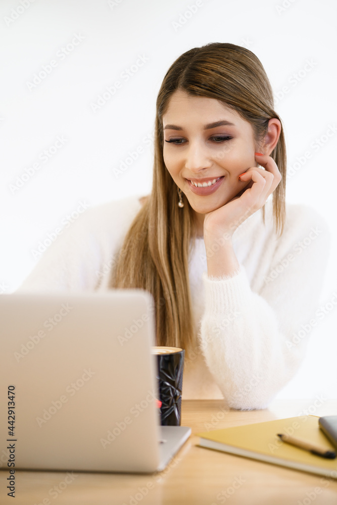 Beautiful young woman in casual clothing using laptop and smiling while working indoors Beautiful young woman in casual clothing using laptop and smiling while working indoors