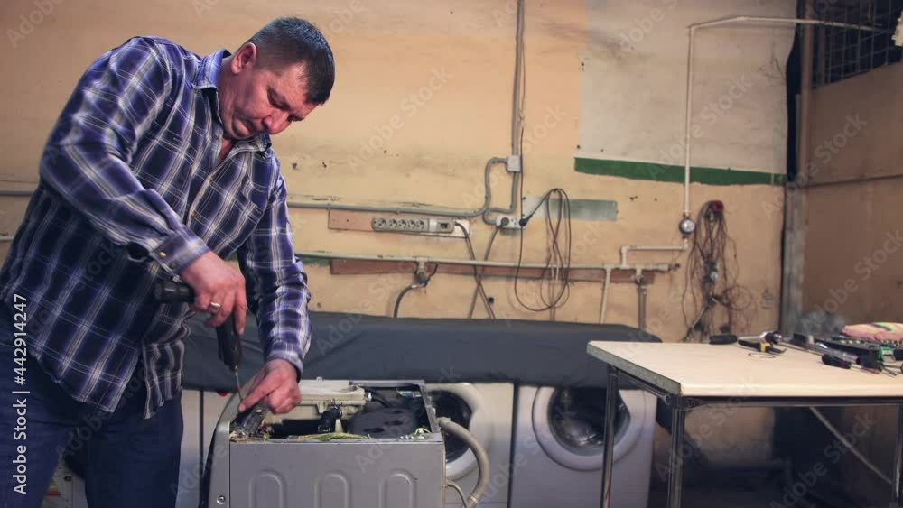 The master uses a screwdriver to fix the front panel with screws. The man disassembles, assembles, repairs the washing machine. Business concept in the field of maintenance and repair services. UHD 4K The master uses a screwdriver to fix the front panel with screws. The man disassembles, assembles, repairs the washing machine. Business concept in the field of maintenance and repair services. UHD 4K