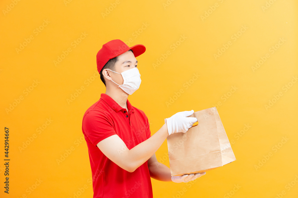 delivery guy hold takeaway package look camera wear mask red t-shirt cap isolated yellow color background delivery guy hold takeaway package look camera wear mask red t-shirt cap isolated yellow color background
