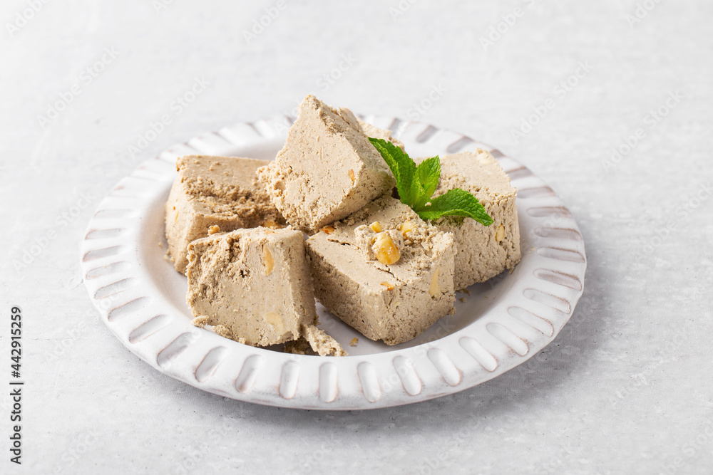 pieces of sunflower halva with peanuts in a gray plate, mint, light gray background, oriental sweets