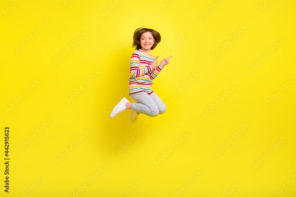 Full body photo of charming cheerful young small girl jump up point finger empty space isolated on yellow color background