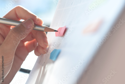Woman hand with a pencil taking note on work planner schedule on desktop calendar  checking appointment date  event planning  close up