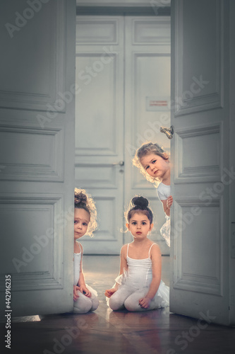 Three funny little ballerinas in tutus are peeking out from behind the door. Image with selective focus and toning
