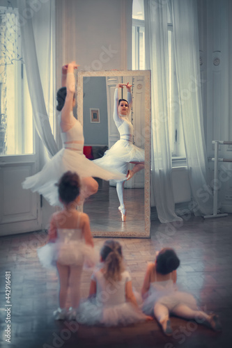 Three little funny ballerinas are looking with delight at dancing adult ballerina. Image with selective focus and toning