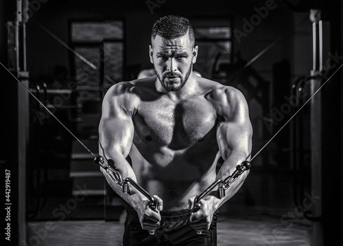 Fitness man execute exercise with exercise-machine Cable Crossover in gym. Handsome man with big muscles in gym. Machine in the gym. Black and white