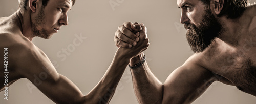 Two man's hands clasped arm wrestling, strong and weak, unequal match. Heavily muscled bearded man arm wrestling a puny weak man photo