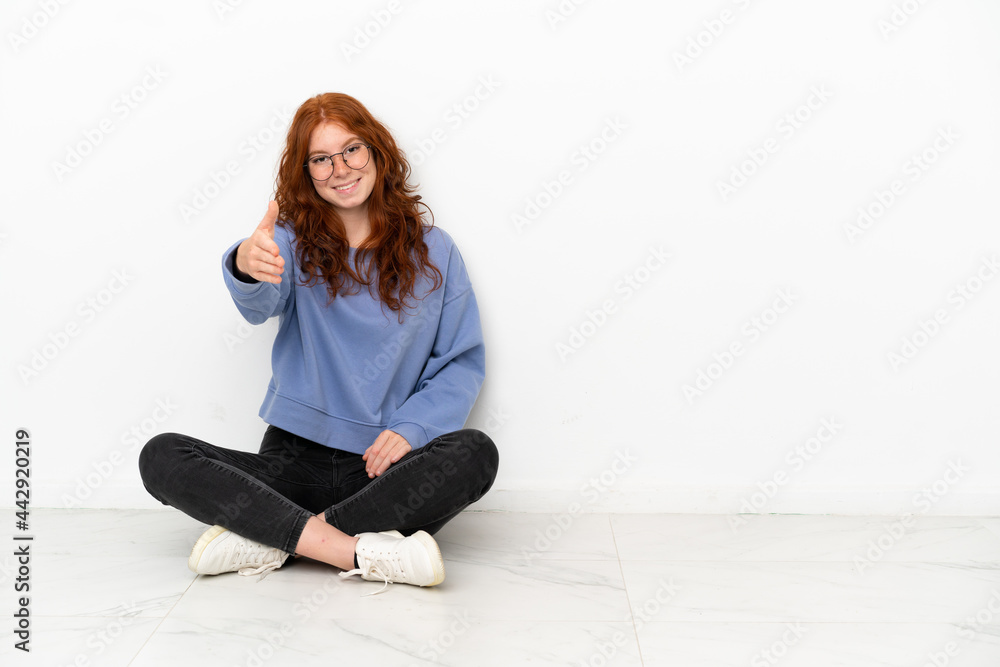 Teenager redhead girl sitting on the floor isolated on white background shaking hands for closing a good deal Teenager redhead girl sitting on the floor isolated on white background shaking hands for closing a good deal