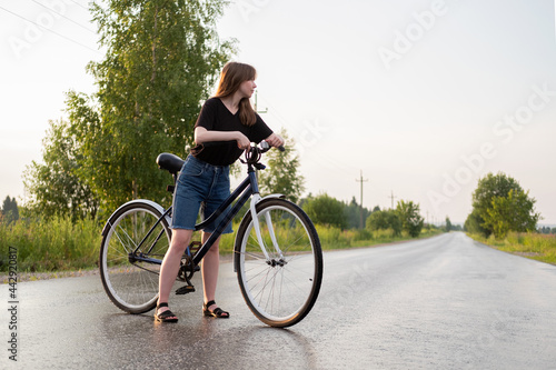 Young woman standing alone on road with bicycle at countryside. Summer activity, healthy lifestyle, workout, sport, fitness. Alone person in nature. Riding bicycle. Having fun outdoors.