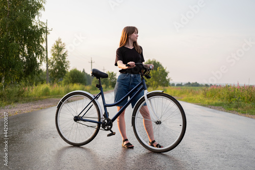 Young woman standing alone on road with bicycle at countryside. Summer activity, healthy lifestyle, workout, sport, fitness. Alone person in nature. Riding bicycle. Having fun outdoors.