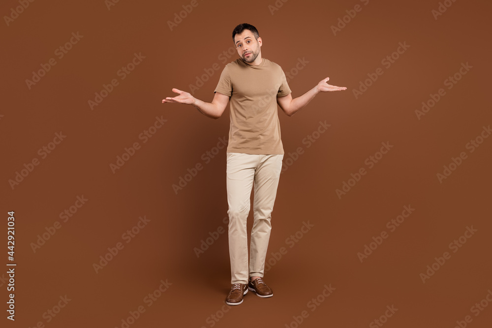 Photo of adorable upset young gentleman wear beige t-shirt not know answer shrugging shoulders isolated brown color background