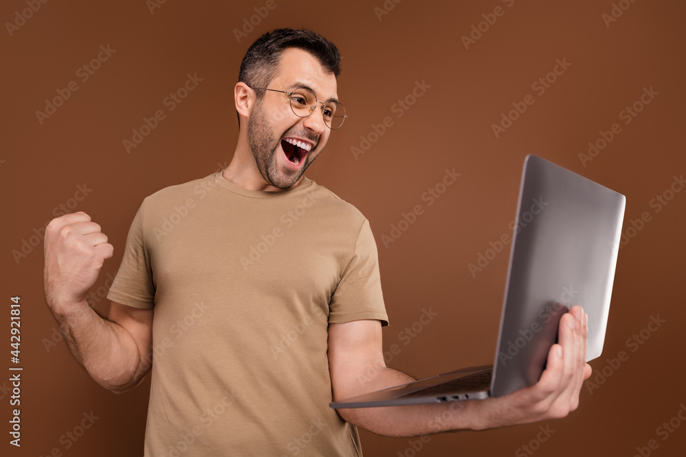Photo portrait brunet man in pastel t-shirt keeping laptop gesturing like winner isolated brown color background Photo portrait brunet man in pastel t-shirt keeping laptop gesturing like winner isolated brown color background