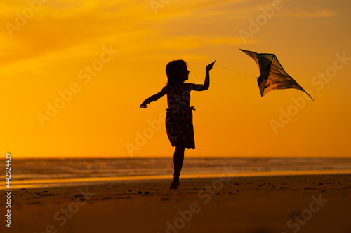 young girl playing with kite on the beach at sunset