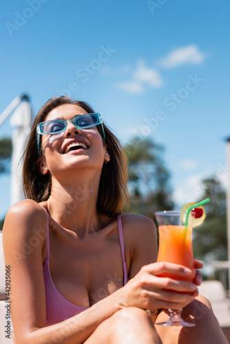 Cheerful woman in swimsuit holding blurred cocktail outdoors