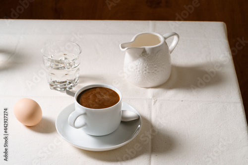 Coffee, boiled egg, milk and glass of water on linen tablecloth, breakfast