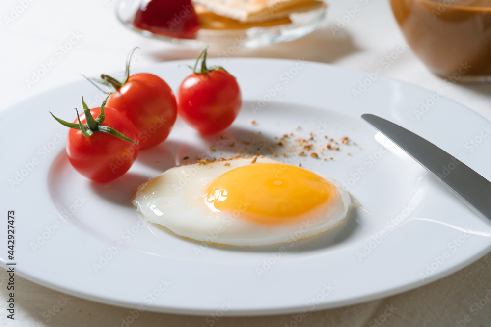 Fried egg with tomatoes on white plate, breakfast dining table Fried egg with tomatoes on white plate, breakfast dining table