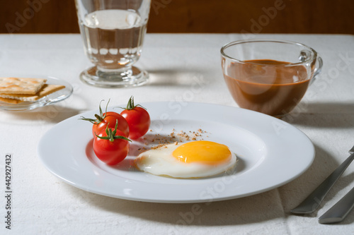 Fried egg with tomatoes on white plate, breakfast dining table