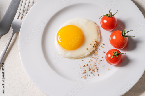 Fried egg with tomatoes on white plate, breakfast dining table