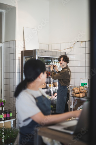 Man pratar med kvinnlig kollega som arbetar på laptop i butik photo