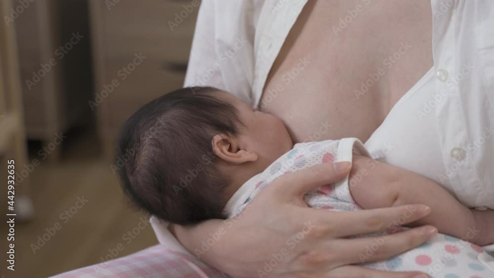 first time mom is deeply attaching her newborn child to her breast and feeding her in tranquility with cropped shot. first time mom is deeply attaching her newborn child to her breast and feeding her in tranquility with cropped shot.