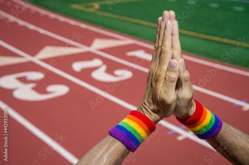 Athlete with gay pride rainbow wrist sweatbands praying with hand together at a running track