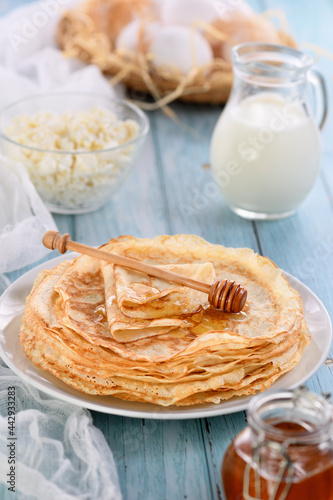  Homemade thin pancakes with honey stacked in a stack, on a wooden table with a mug of milk, a pot of sour cream and eggs in a basket. Traditional Slavonian, pagan holiday (Maslinitsa). Country style  photo